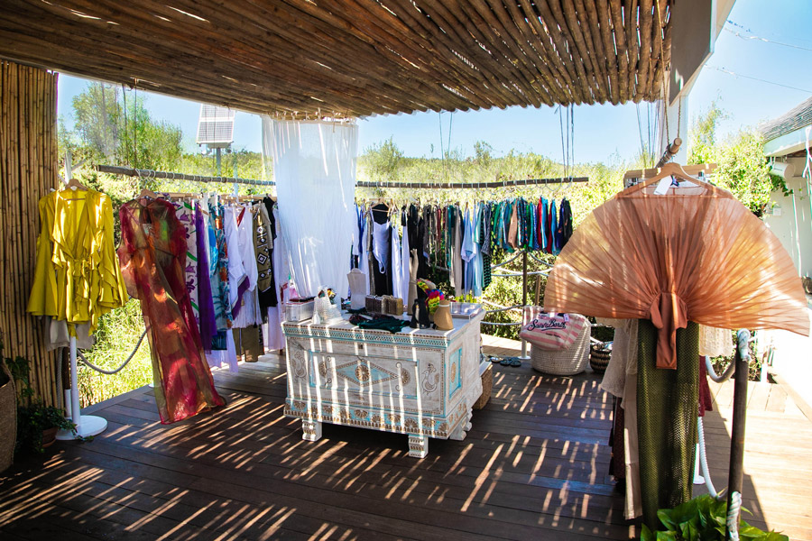 Image of a Luxury Pop Up in Sardinia, at Nikki Beach in Costa Smeralda. In the foreground the "follow the sun" sign indicating the pop up, and hangers with colorful clothes and accessories